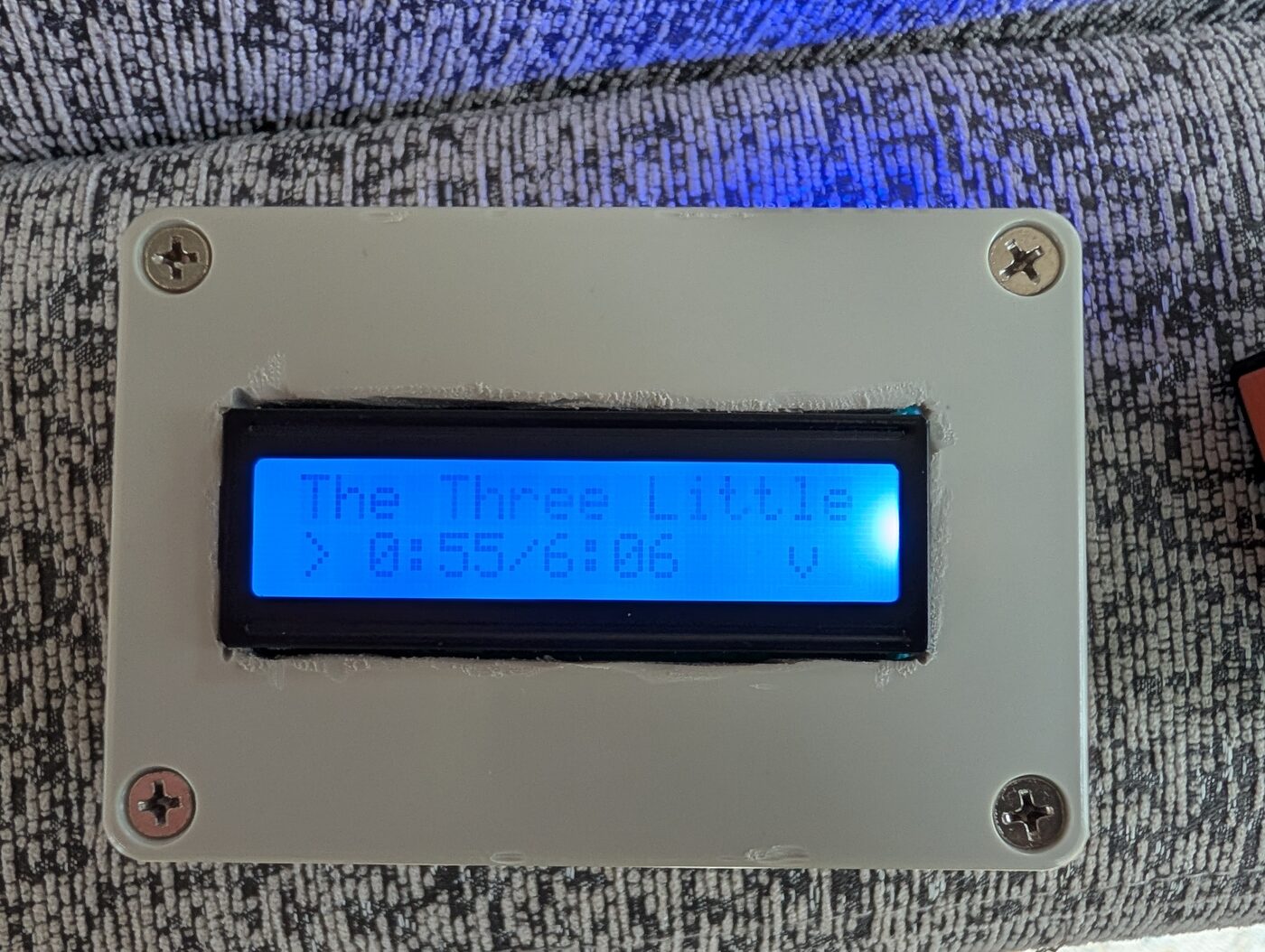 Close-up of the LCD reading 'The Three Little' with a playback timer of 0:55 / 6:06 and a heart.